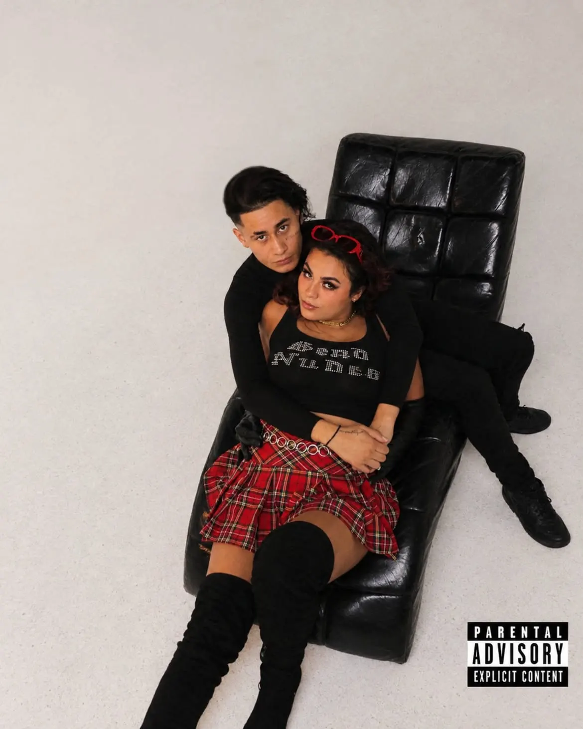Twenty-One cover art: John Caicedo and a woman in a red plaid skirt on a black leather lounge chair